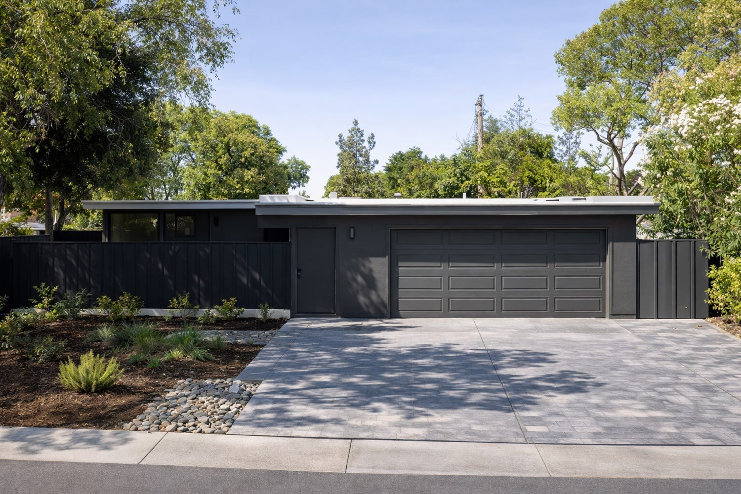 Charcoal-painted Eichler in Cupertino with board-and-batten siding, a dark privacy fence, and a paver driveway