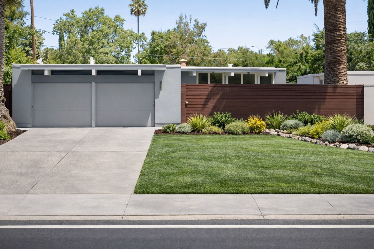 Grey-painted Eichler behind a mahogany horizontal fence, with a green lawn and a drought-tolerant planting border